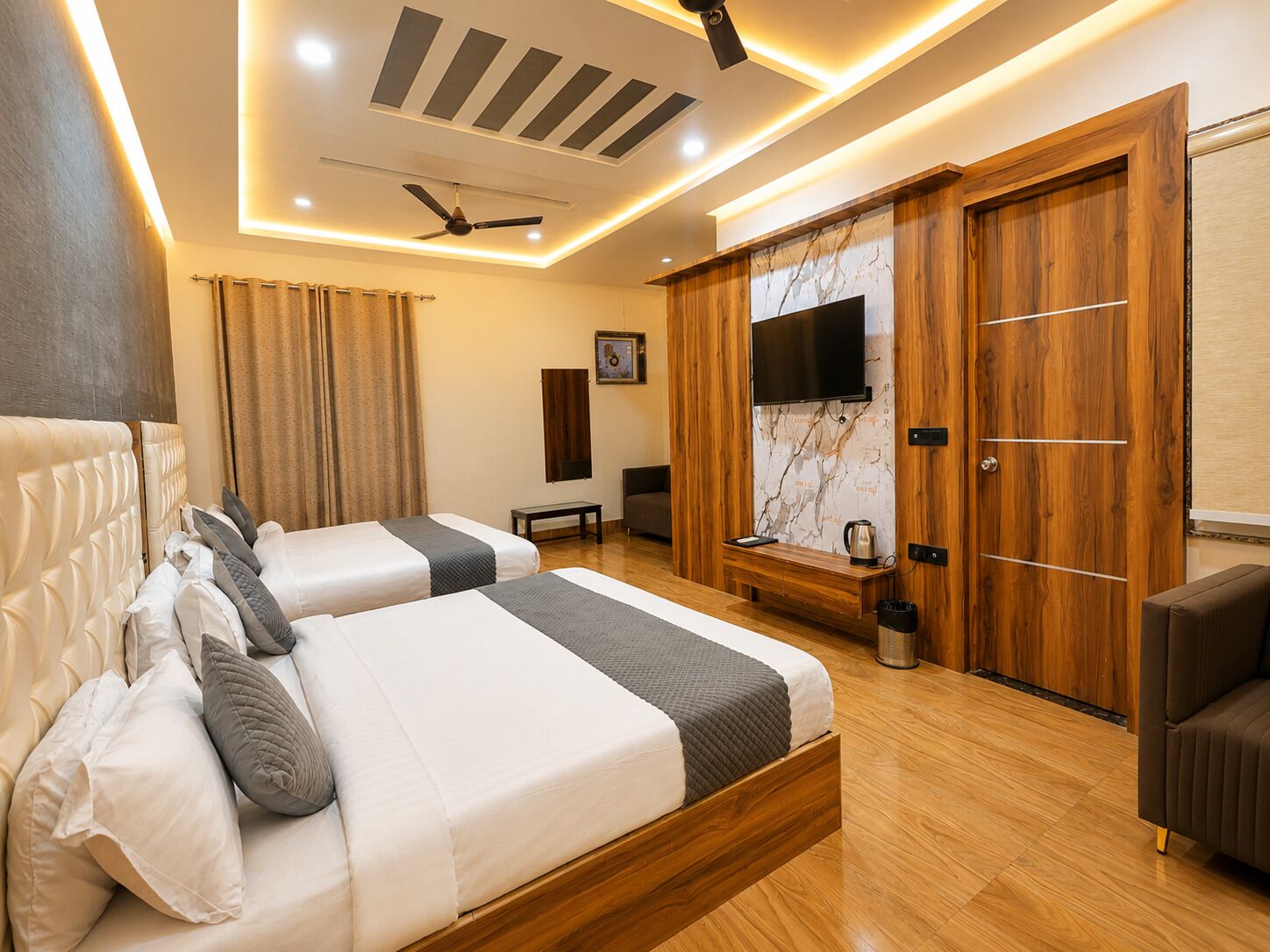 A hotel room with two beds, a TV, a ceiling fan, and wooden furniture.