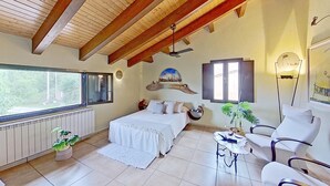 A bedroom with a bed, a chair, a table, a radiator, a window, and a ceiling fan.