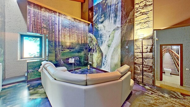 A room with a large mural of a forest and waterfall, a stone wall, and a glass table with a chair.