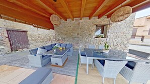 An outdoor patio with wicker furniture, a stone wall, and a wooden ceiling.