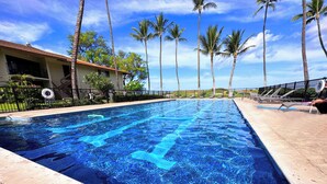 Una piscina con agua cristalina azul, rodeada de palmeras y una cerca.
