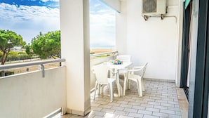 Un balcon avec une table et des chaises blanches, un appareil de climatisation et une vue sur la plage.