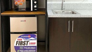 A compact kitchen with dark wooden cabinets, a built-in microwave, a small refrigerator, and a countertop with a sink. - Cozy Condo in Mandaluyong City, Metro Manila (Mandaluyong)