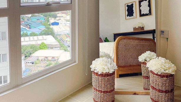 A room with a large window, a mirror, wicker baskets with flowers, and a wicker chair. - Cozy Condo in Mandaluyong City, Metro Manila (Mandaluyong)