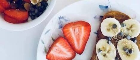 A breakfast setting with a plate of toast topped with banana slices and strawberries, a bowl of granola with nuts and seeds, and a glass of orange juice.
