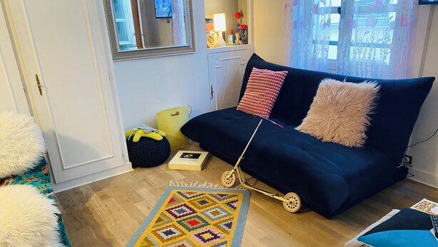 Un salon chaleureux avec un canapé bleu foncé, un tapis à motifs et une petite table sur laquelle repose un livre.