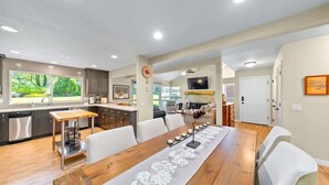 A modern kitchen with stainless steel appliances, a dining area with a wooden table and white chairs, and a living area with a sofa and TV. - Perfect in the Pines - 38 Aspen Circle (Plumas Eureka)