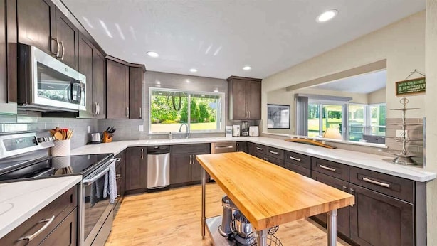 A modern kitchen with dark wood cabinets, stainless steel appliances, and a large window providing natural light. - Perfect in the Pines - 38 Aspen Circle (Plumas Eureka)