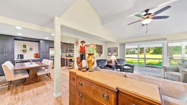 A spacious living room with a large window, a dining area with a wooden table and chairs, and a kitchen area with dark cabinets and a white countertop. - Perfect in the Pines - 38 Aspen Circle (Plumas Eureka)