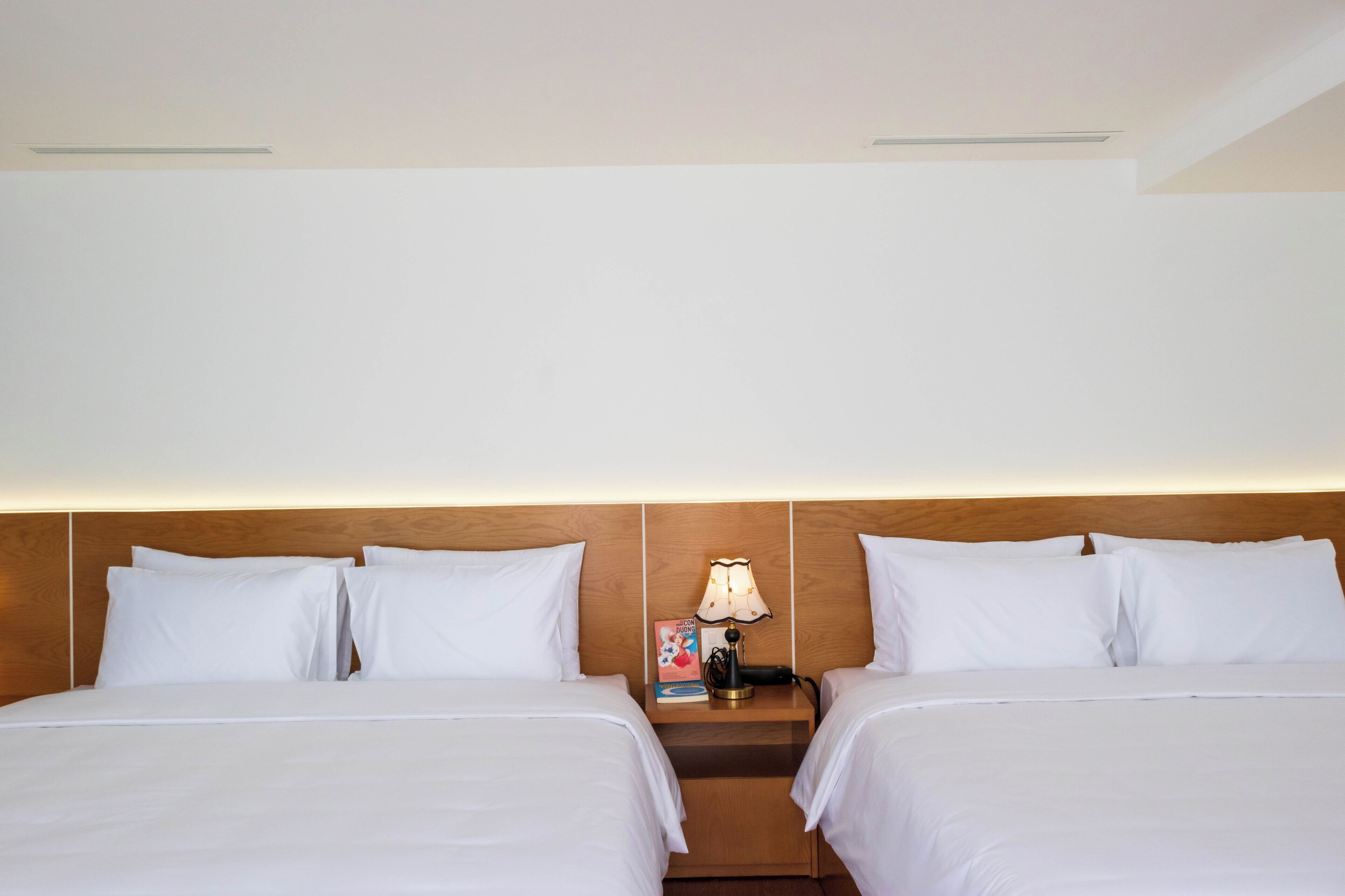 Une chambre d’hôtel avec deux lits, une table de chevet avec une lampe et un livre.
