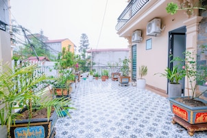 Un patio con plantas en macetas, suelo de baldosas y unidades de aire acondicionado en las paredes.