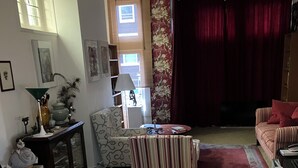 A living room with a sofa, armchair, and a coffee table. There is a window with blinds, a lamp, and a vase on a side table.
