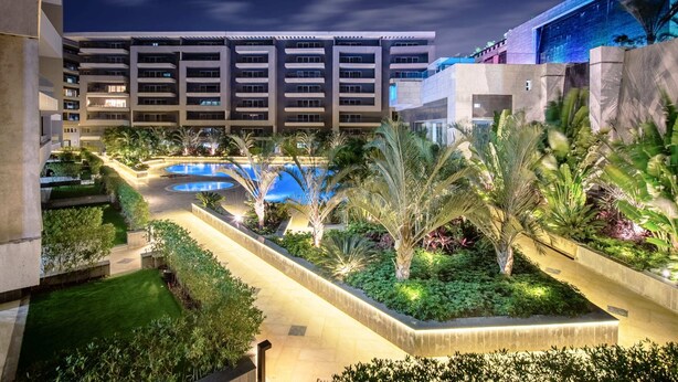 Un hotel moderno con piscina, abundante vegetación y un patio bien iluminado.