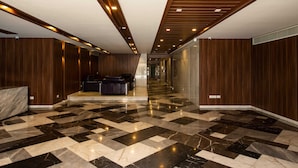 Un vestíbulo de hotel con suelo de mármol a cuadros, paneles de madera en las paredes y un mostrador de recepción con asientos de cuero.