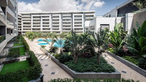 Un patio moderno de hotel con piscina, abundante vegetación y un edificio de varios pisos al fondo.