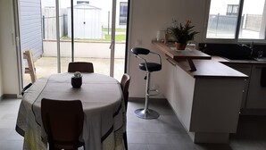 Une cuisine compacte comprenant un coin repas, un petit comptoir-bar et une vue sur le jardin à travers une porte-fenêtre coulissante.