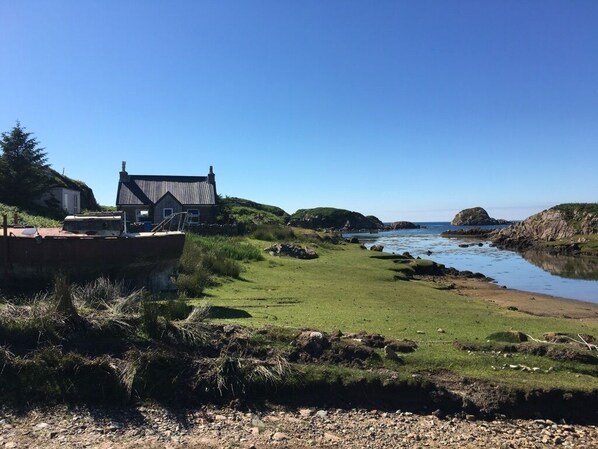 A coastal scene with a house, grassy area, and calm water.