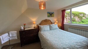 A bedroom with a bed, a nightstand, a dresser, a window with a view of greenery, and a ceiling light fixture. - Idyllic Hebridean Island Retreat (Kintra)