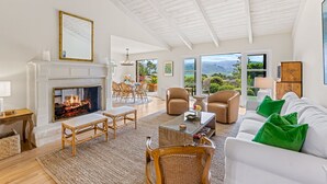 Amplio salón con chimenea, asientos cómodos y ventanas grandes que ofrecen vistas al exterior.