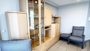 A room with a wooden cabinet with glass doors, two grey upholstered chairs, and a tiled floor. - Apartment in Wenduine With Stunning Sea Views (De Haan)