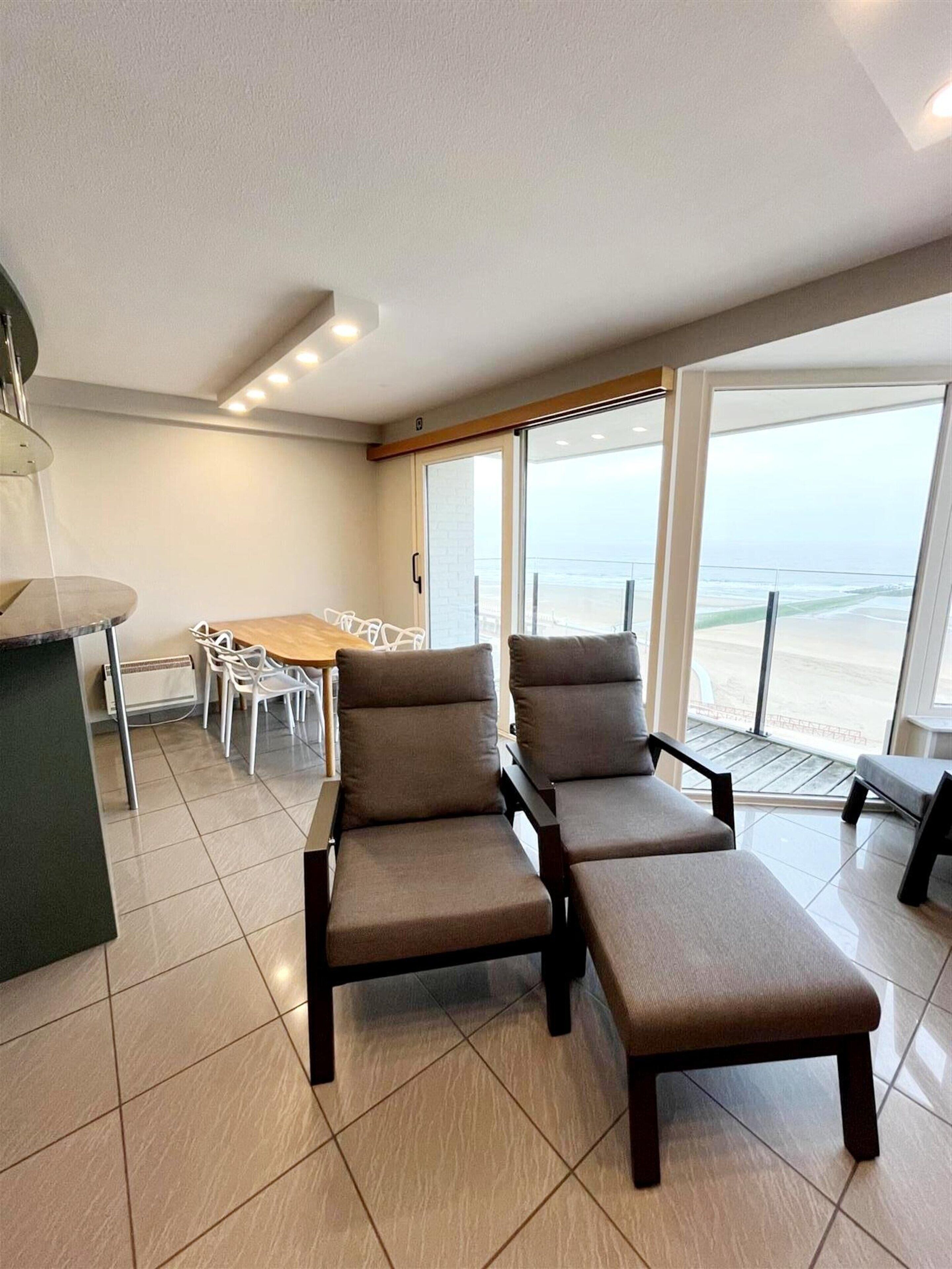 Un salon moderne avec un balcon donnant sur la plage, un coin repas et une cuisine.