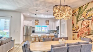 A modern kitchen with white cabinets, a stainless steel refrigerator, and a dining area with a wooden table and grey upholstered chairs.