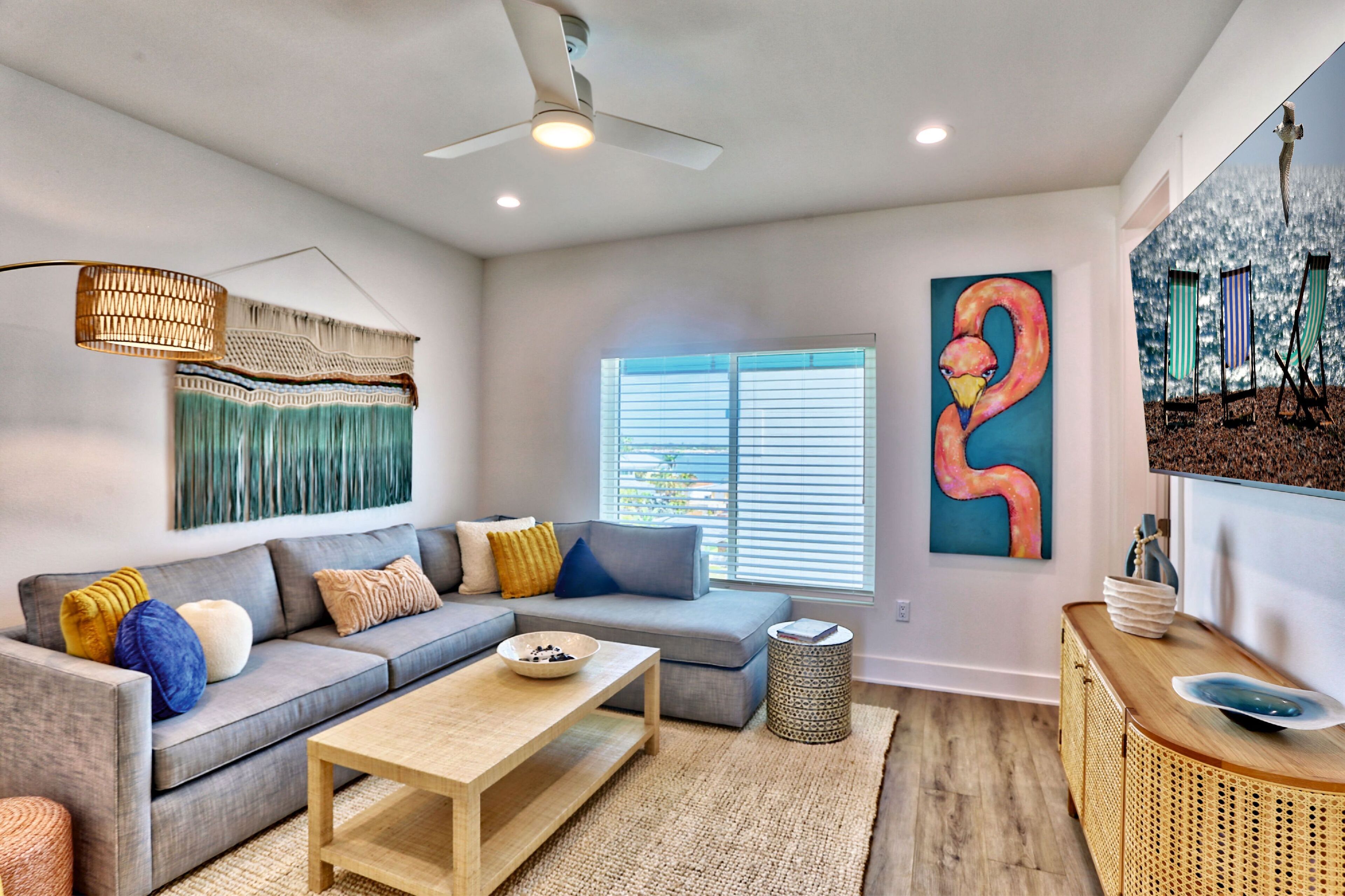 A modern living room with a grey sofa, a wooden coffee table, and a large window with blinds.