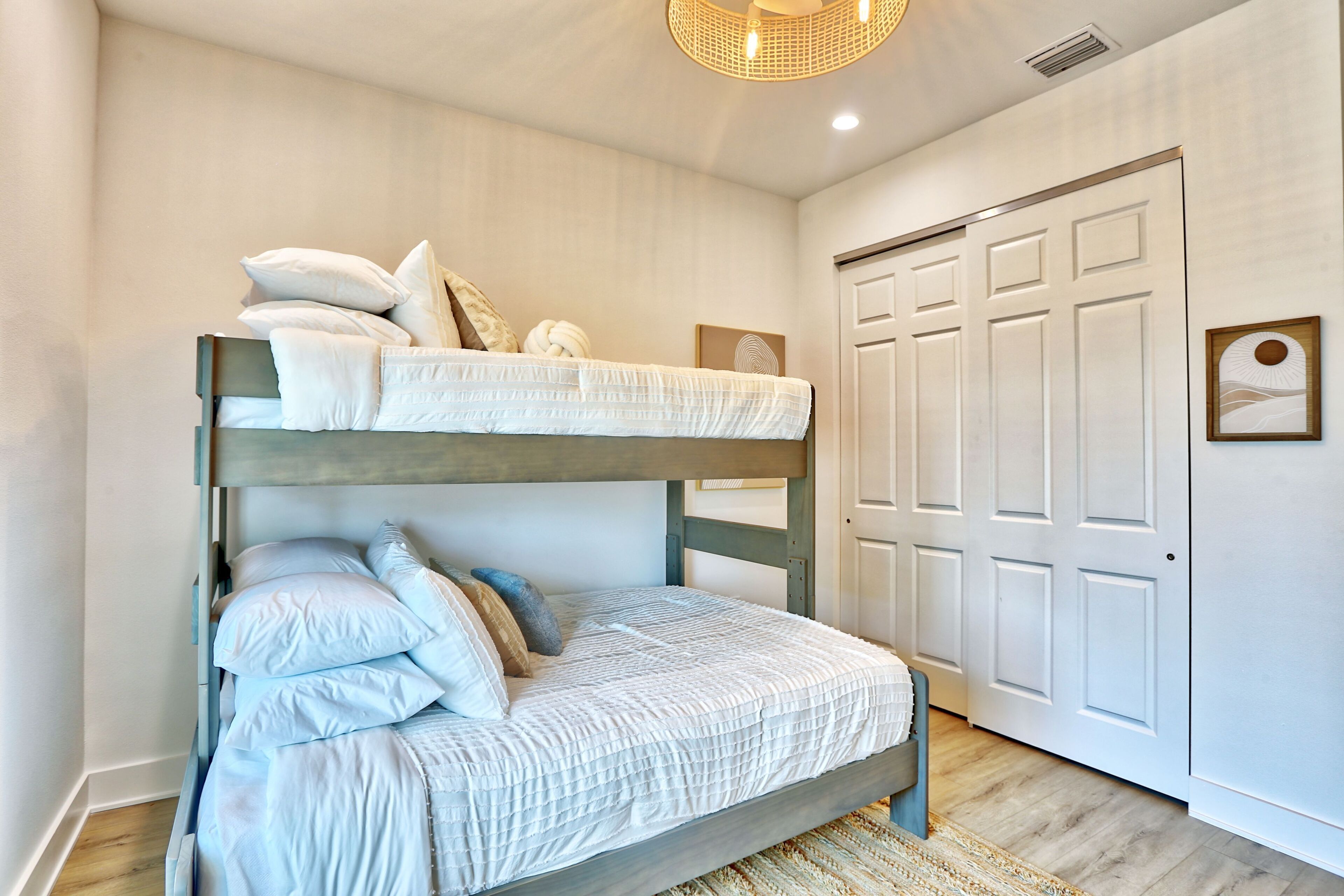 A bunk bed with white bedding and pillows, a wooden headboard, a woven light fixture, and a white door with panels.
