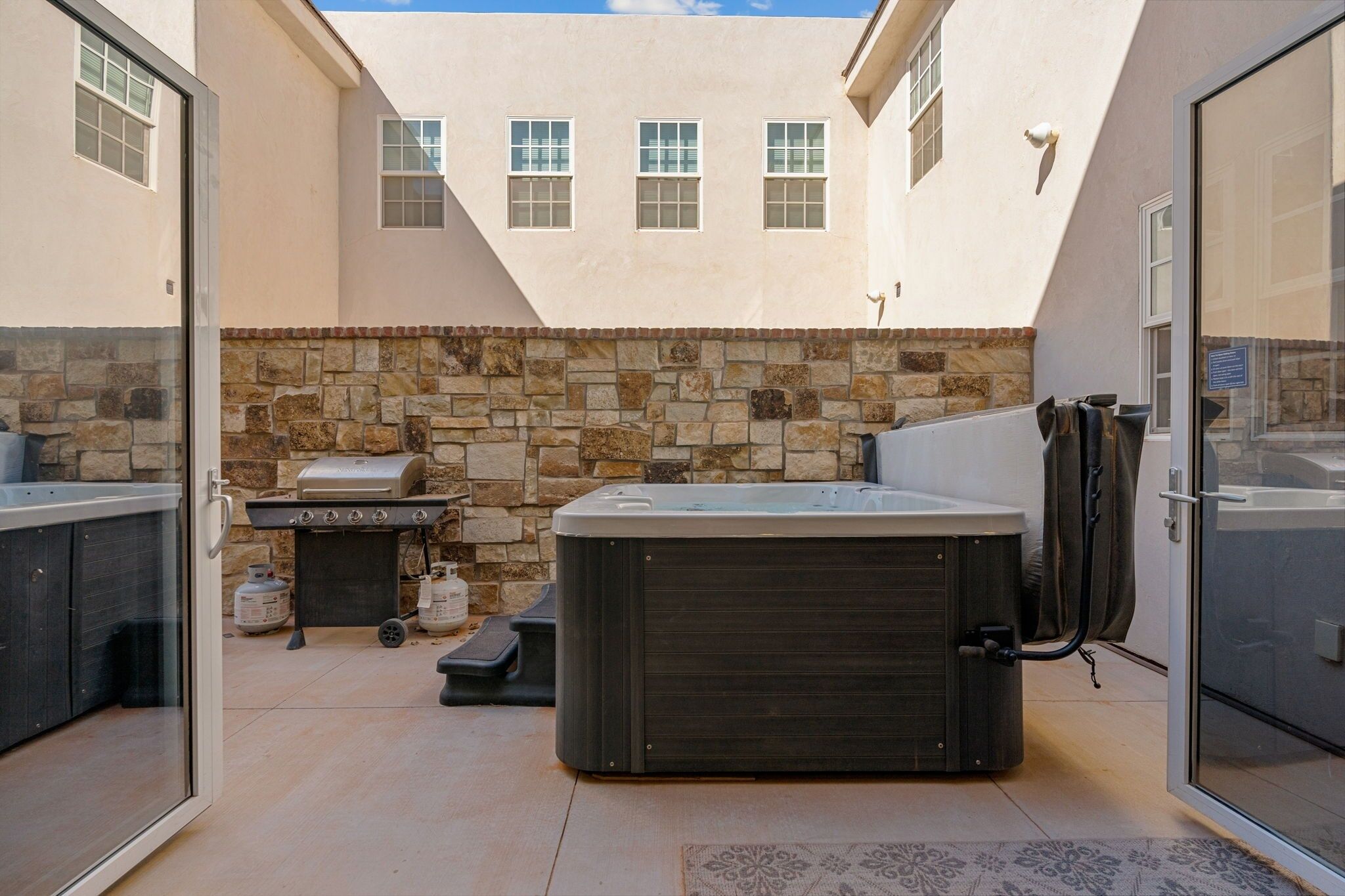 A patio area with a hot tub, grill, and stone wall.
