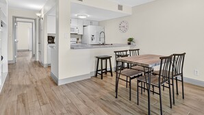 A modern kitchen with white cabinets, a wooden dining table, and a built-in island with bar stools. - Beauty By The Bay K702 1 Bedroom Condo (Rockport)