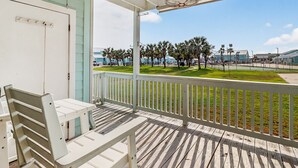 A wooden deck with a white railing, a bench, and a view of a coastal area with palm trees and buildings. - Beauty By The Bay K702 1 Bedroom Condo (Rockport)