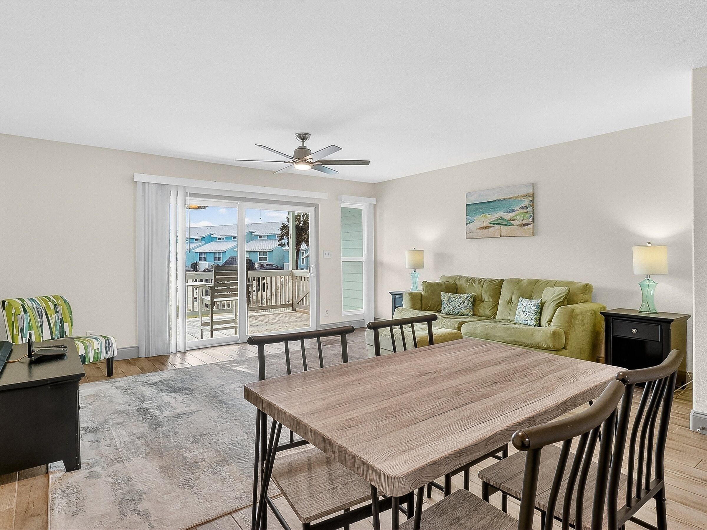 A spacious living room with a wooden dining table, green sofa, and a balcony with a view of houses.