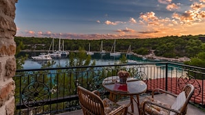 A balcony with wicker chairs and a table, overlooking a marina with boats and a lake, with trees and a rocky landscape in the background. - Hidden Heaven Private Resort - Heated Pool (Milna)