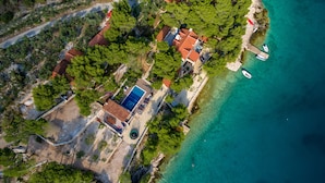 An aerial view of a coastal property with a swimming pool, terraced roofs, and boats docked near the shore. - Hidden Heaven Private Resort - Heated Pool (Milna)