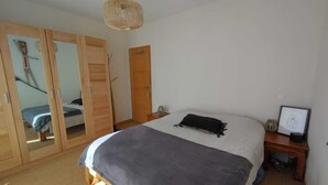 A bedroom with a bed, a wooden wardrobe, a small bedside table, and a hanging light fixture. - Quiet house 200 m from the ocean. (Lacanau)