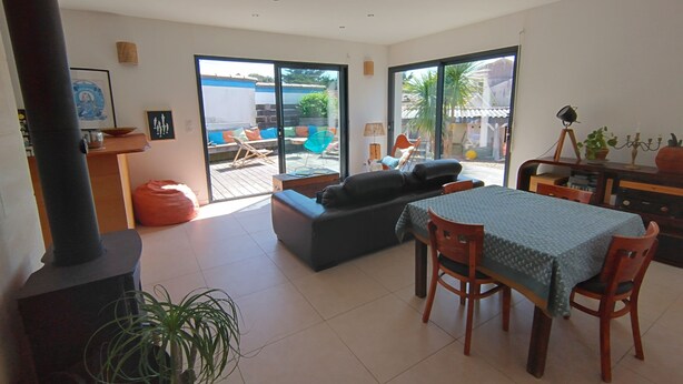 A modern living room with a sofa, a dining table, and chairs. There is a large window providing a view of the outside. - Quiet house 200 m from the ocean. (Lacanau)
