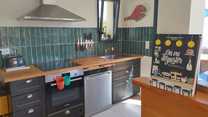 A modern kitchen with a stainless steel range hood, a wooden countertop, a built-in oven, and a dishwasher. - Quiet house 200 m from the ocean. (Lacanau)