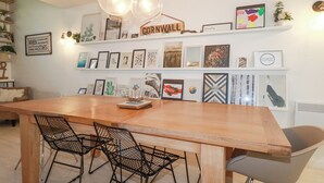 A dining area with a wooden table, black wire mesh chairs, and a grey upholstered chair. - Tincroft (Truro)