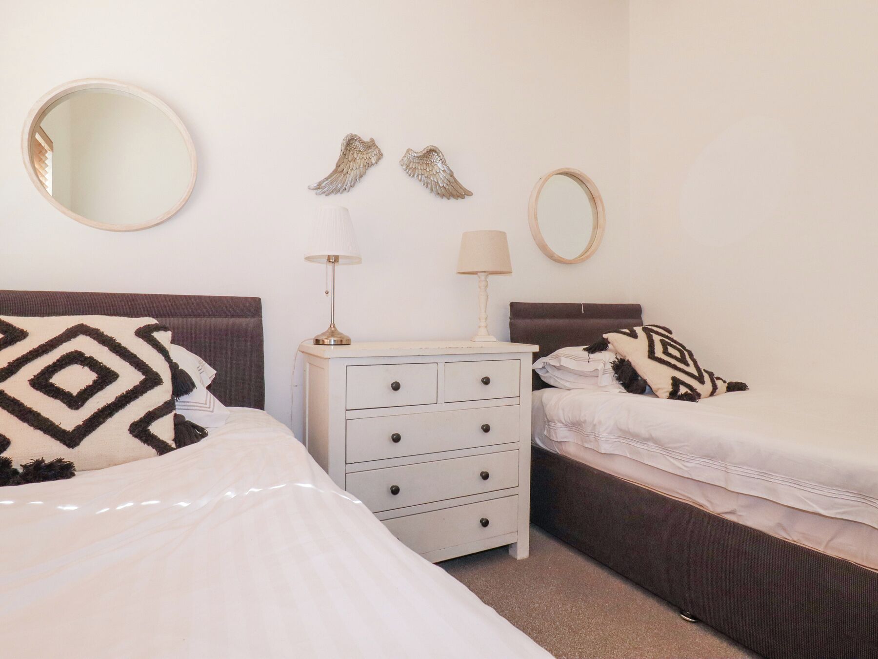 Un dormitorio con dos camas, una mesita de noche, un aparador y espejos decorativos en la pared.