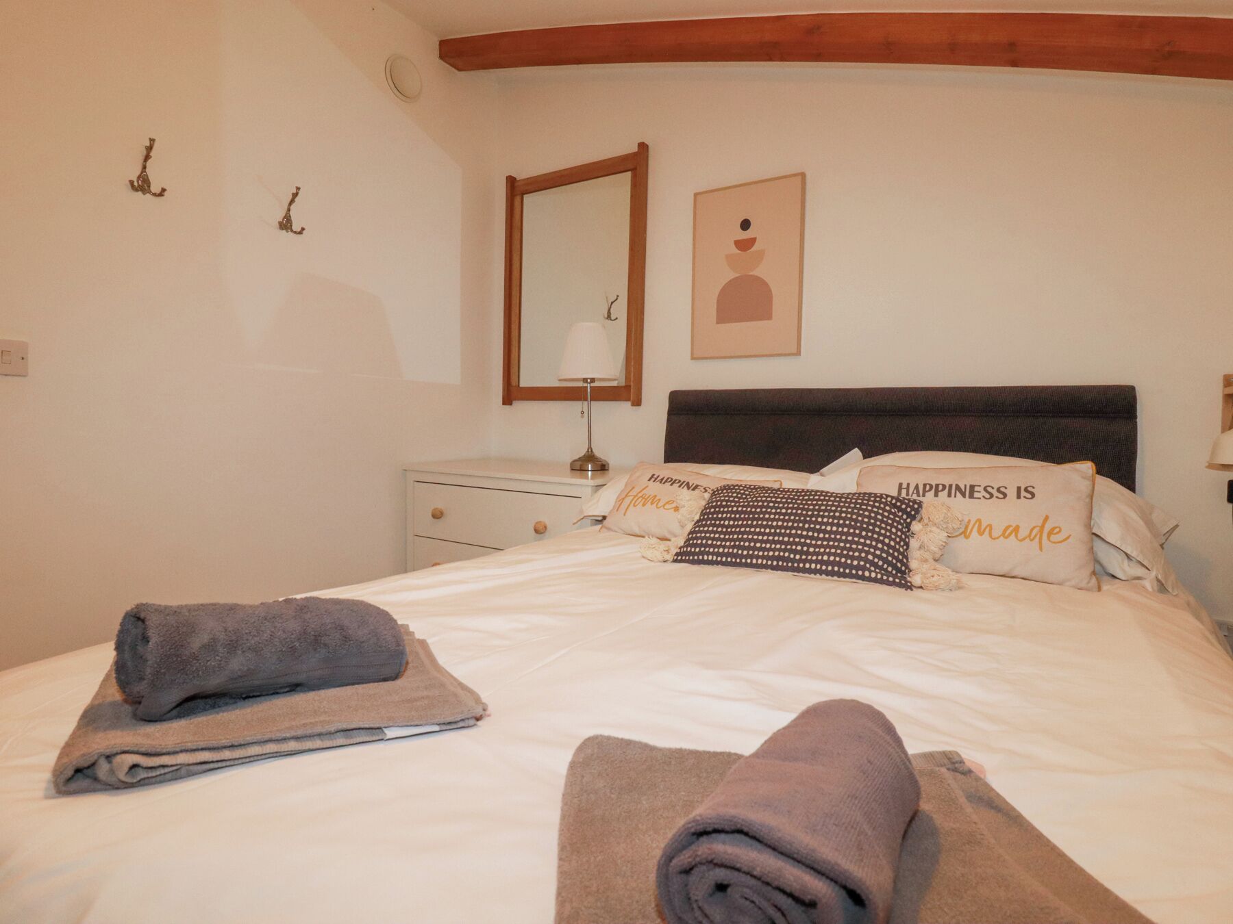 A neatly made bed with rolled towels, a bedside table with a lamp, and a wall with a mirror and a framed picture.