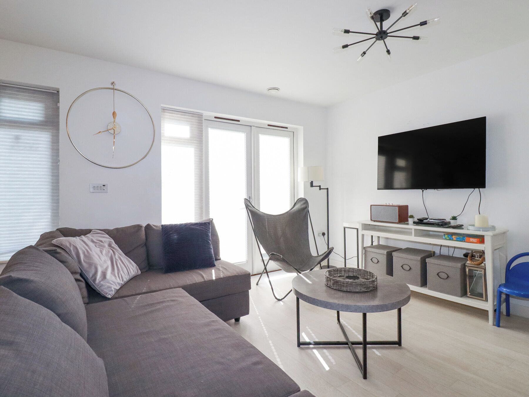 A modern living room with a grey sofa, a round coffee table, a TV on a white stand, and a ceiling light fixture.