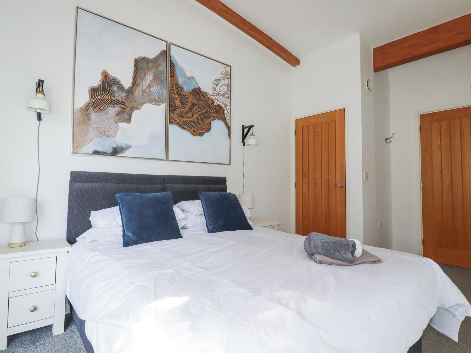 A neatly made bed with white and blue bedding, a bedside lamp, and a wall-mounted light fixture.