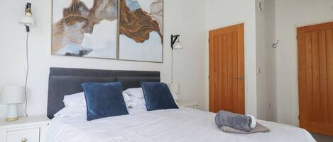 A neatly made bed with white and blue bedding, a bedside lamp, and a wall-mounted light fixture.