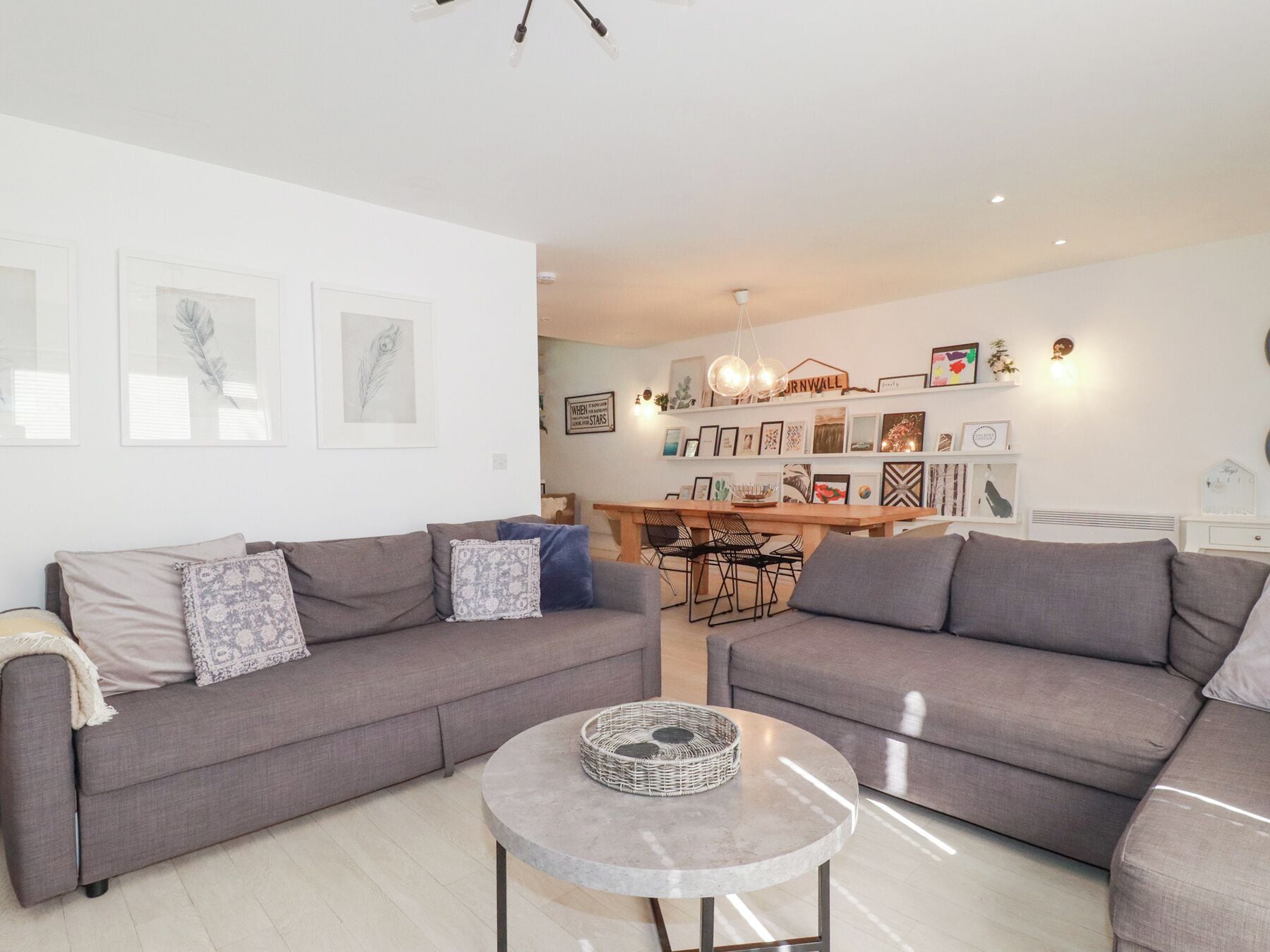 A modern living room with two grey sofas, a round coffee table, and a dining area with a wooden table and chairs.