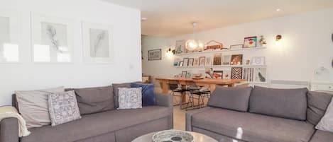 A modern living room with two grey sofas, a round coffee table, and a dining area with a wooden table and chairs.