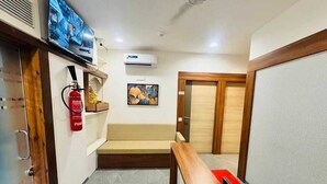 Um hall de hotel com um banco de madeira, um extintor de incêndio, uma televisão presa na parede e uma porta com moldura de madeira.