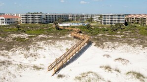 A beachfront hotel with multiple buildings, a sandy beach, and a wooden boardwalk.