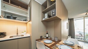 A compact kitchen with a sink, stove, and shelves. A dining table with plates and cutlery is set for two. - Modern 1Bedroom,1 bathroom,Terrace,Wash/Dry and WiFi 8min MetroL5 Santiago (Santiago)