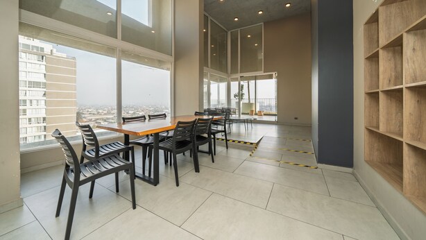 A spacious room with a large table and chairs, large windows offering a city view, and a wooden shelving unit. - Modern 1Bedroom,1 bathroom,Terrace,Wash/Dry and WiFi 8min MetroL5 Santiago (Santiago)
