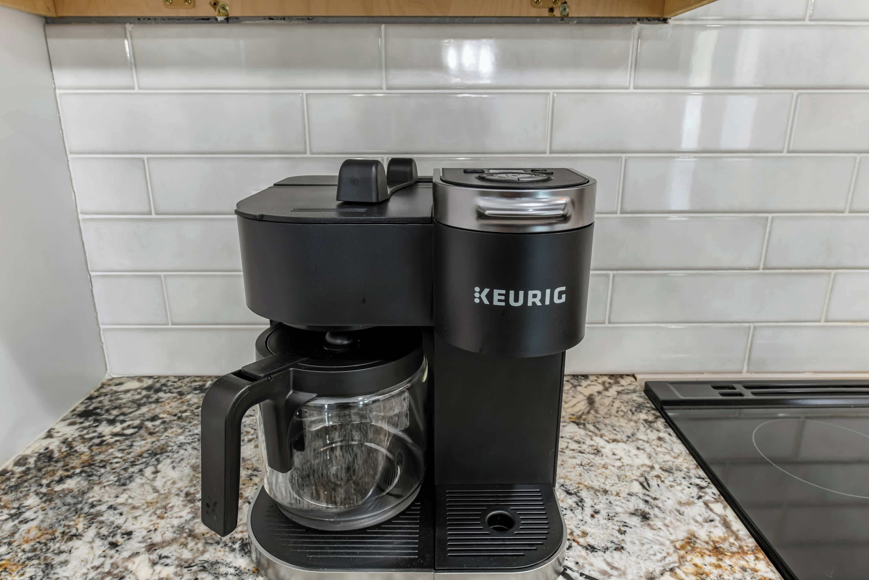 A Keurig coffee maker on a granite countertop with a white tiled backsplash.